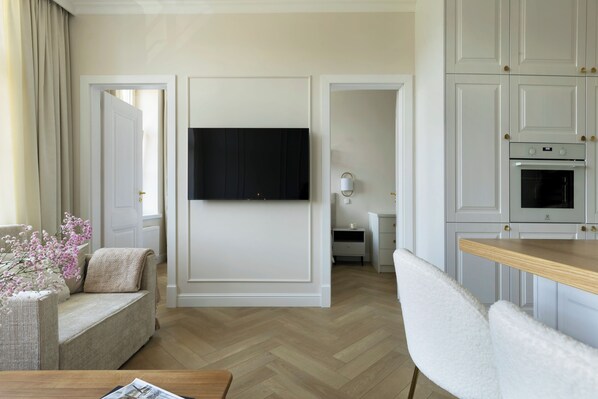 A modern living room with a sofa, a coffee table, a TV mounted on a wall, and a kitchen area with cabinets and a microwave. - Elite Apartments Dobra Premium (Gdansk)