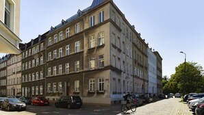 En flervåningsbyggnad med en entré på hörnet, parkerade bilar och en cyklist.