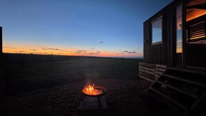 Une cabane avec un foyer au premier plan et une vue sur le coucher de soleil en arrière-plan.