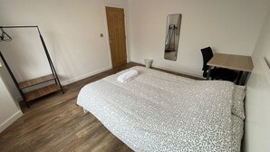 Een slaapkamer met een bed, een houten vloer, een kledingkast, een deur en een spiegel aan de muur.