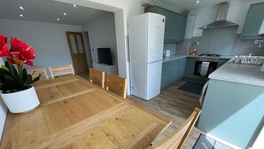 Een moderne keuken met een houten eettafel, een witte koelkast en lichtblauwe kastjes.