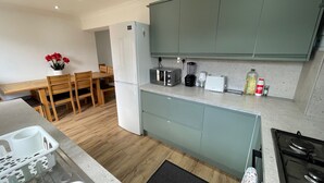 Een moderne keuken met grijze kastjes, een eetgedeelte met houten stoelen, en een klein eiland met een spoelbak en kookplaat.