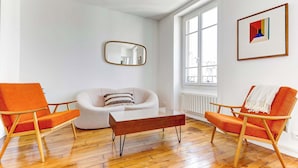 Un salon moderne avec un plancher en bois, un canapé blanc et deux fauteuils orange.