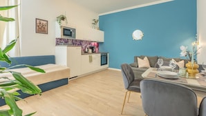 Una sala moderna con una pared azul de acento, un comedor con una mesa preparada para dos personas y una kitchenette con microondas y horno.