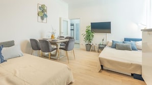 Una habitación moderna y bien iluminada con dos camas, una zona de comedor y un televisor.