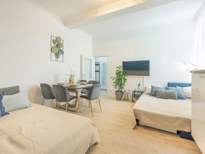 A modern, well-lit room with two beds, a dining area, and a TV.