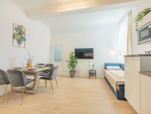 A modern, well-lit room with a dining area, a bed, a TV, and a small table with a plant.