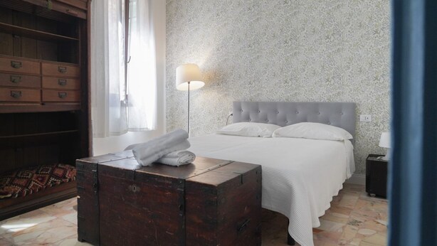 A bedroom with a bed, a wooden chest, a lamp, and a wardrobe. - Apartment in the center of Venice (Venezia)