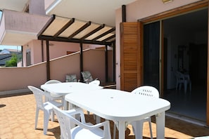 A patio with a white table and chairs, a pergola, and a sliding glass door leading to an interior space.