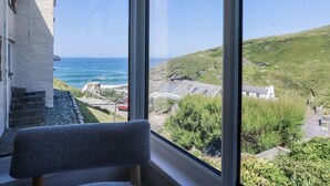 Une pièce dotée d’une grande fenêtre donnant sur un paysage côtier, avec vue sur la mer et une colline parsemée de bâtiments.