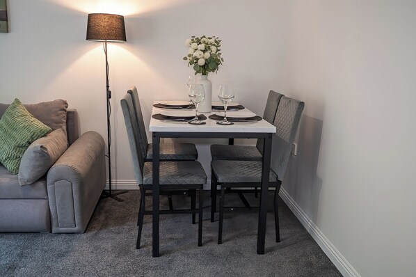 A dining area with a table set for four, a vase of flowers, and a floor lamp.