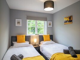 A bedroom with two beds, a window, a lamp, and a painting.
