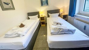 Camera d'albergo con due letti singoli, un comodino con una lampada, un quadro appeso al muro e una finestra con tende.