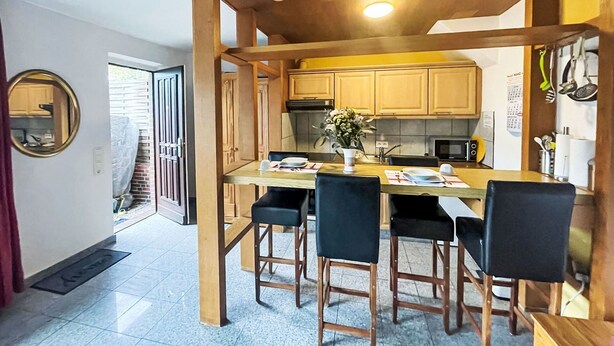 A compact kitchen with wooden cabinets, a central island with bar stools, a microwave, and a small refrigerator. - Lovely apartment for 2 people with WIFI, TV, patio and pets allowed (Westerland)