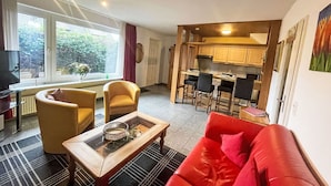 A compact living space with a sofa, chairs, a coffee table, a TV, and a kitchen area with bar stools. - Lovely apartment for 2 people with WIFI, TV, patio and pets allowed (Westerland)