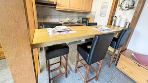 A compact kitchen with wooden cabinets, a microwave, and a sink. There are four black chairs around a wooden table. - Lovely apartment for 2 people with WIFI, TV, patio and pets allowed (Westerland)