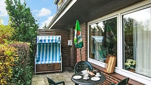 A patio with a table set for two, a striped umbrella, and a brick wall. - Lovely apartment for 2 people with WIFI, TV, patio and pets allowed (Westerland)