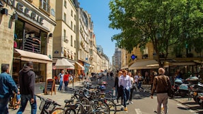 Une rue animée en ville, bordée de cafés, de boutiques et où l’on voit des vélos garés.