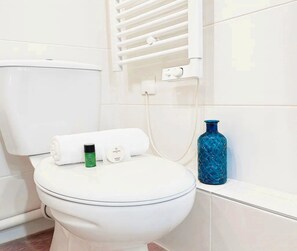 Sanitário branco com toalha, uma garrafa verde e um vaso azul ao lado.