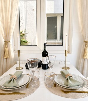 A dining table set with plates, glasses, a bottle, and candles, with a window and curtains in the background. - 1571 Lombards (Paris)