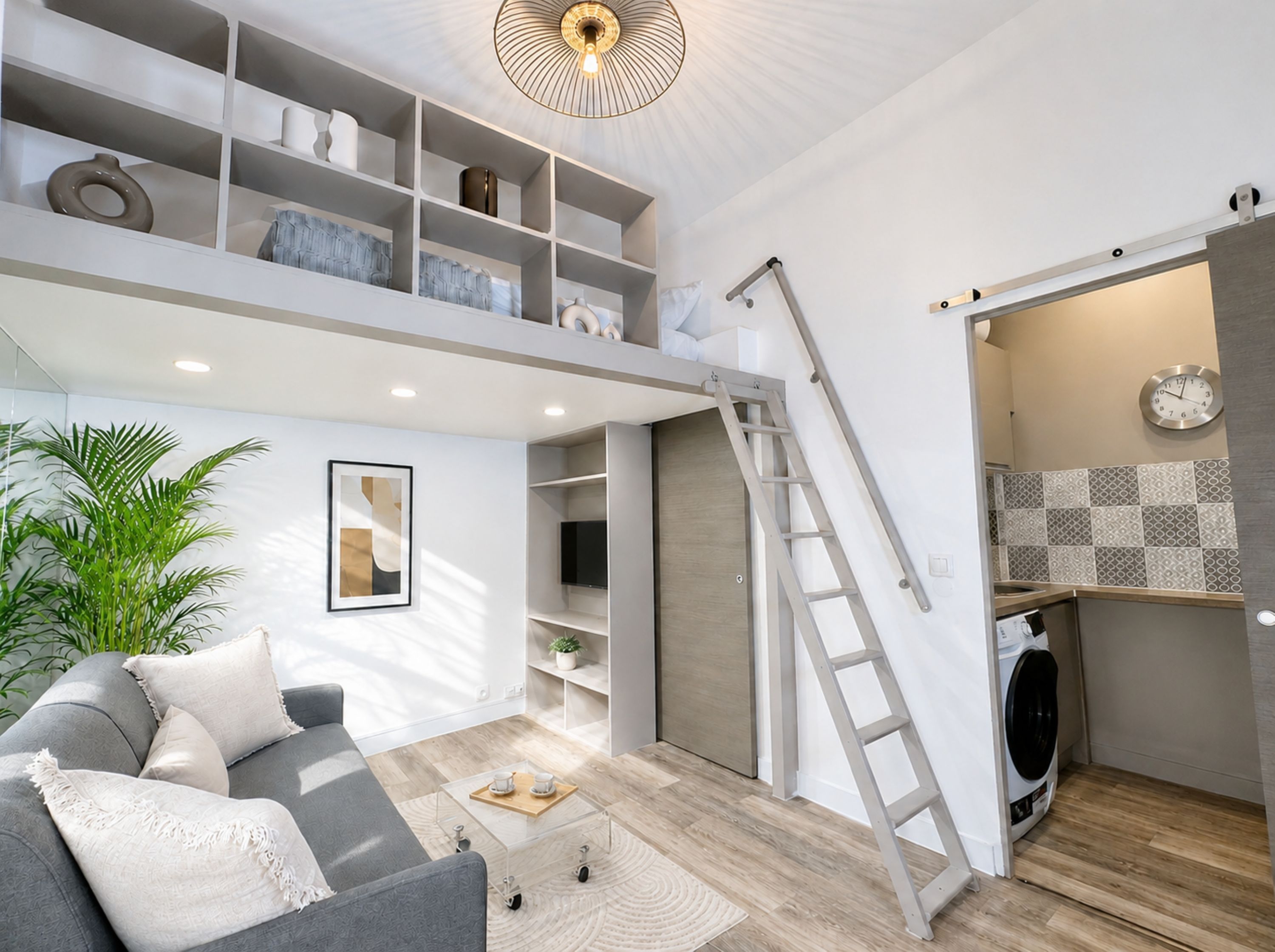 Un espace de vie moderne avec un canapé gris, une table basse, une échelle et un lave-linge et un sèche-linge intégrés.