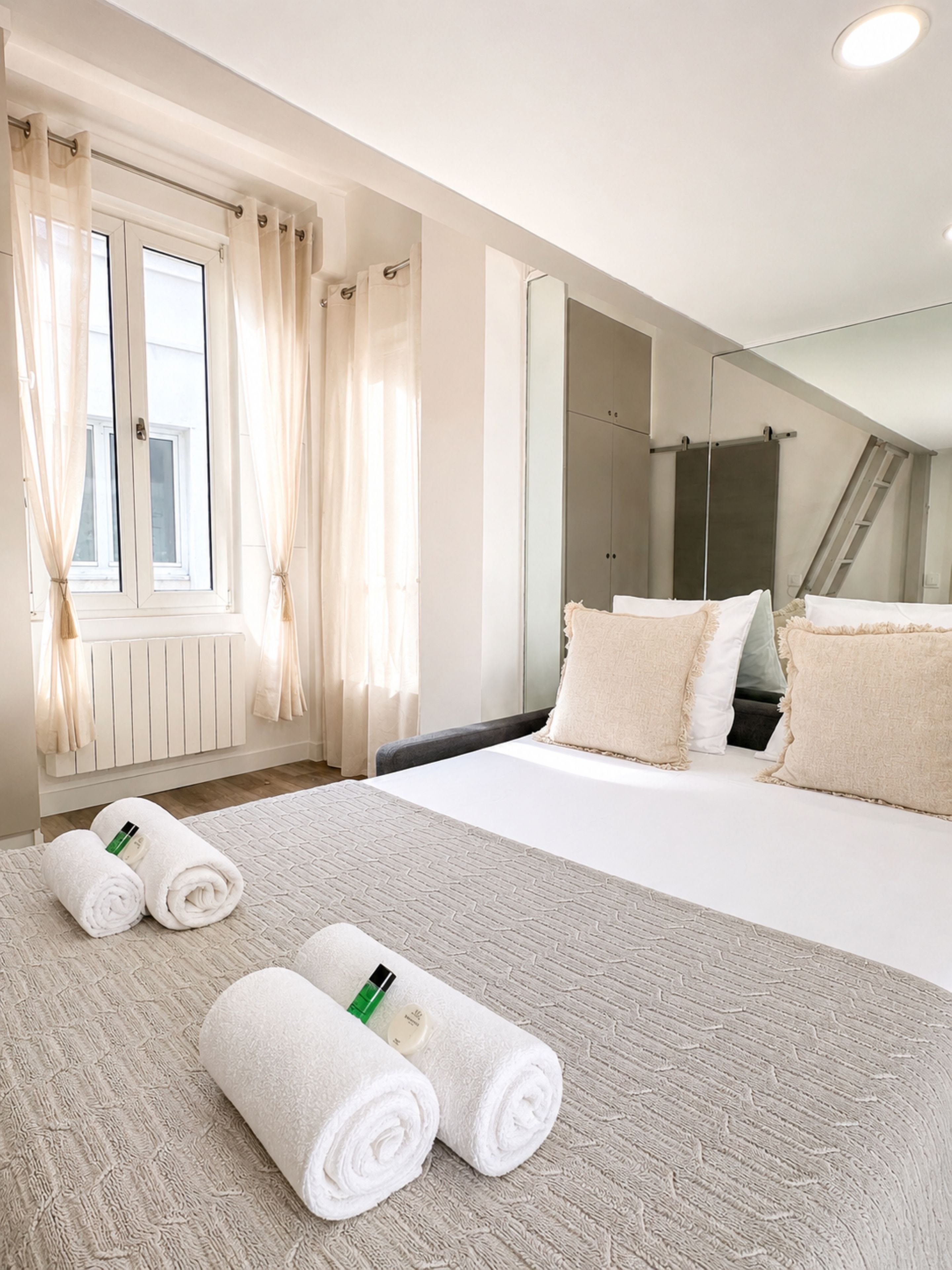 Ein Hotelzimmer mit Bett, Handtüchern, einem fenster mit Vorhängen, einem Spiegel und einer Duschkabine.