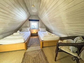 Accogliente camera da letto in soffitta con due letti, una finestra, una lampada e una poltrona in vimini.
