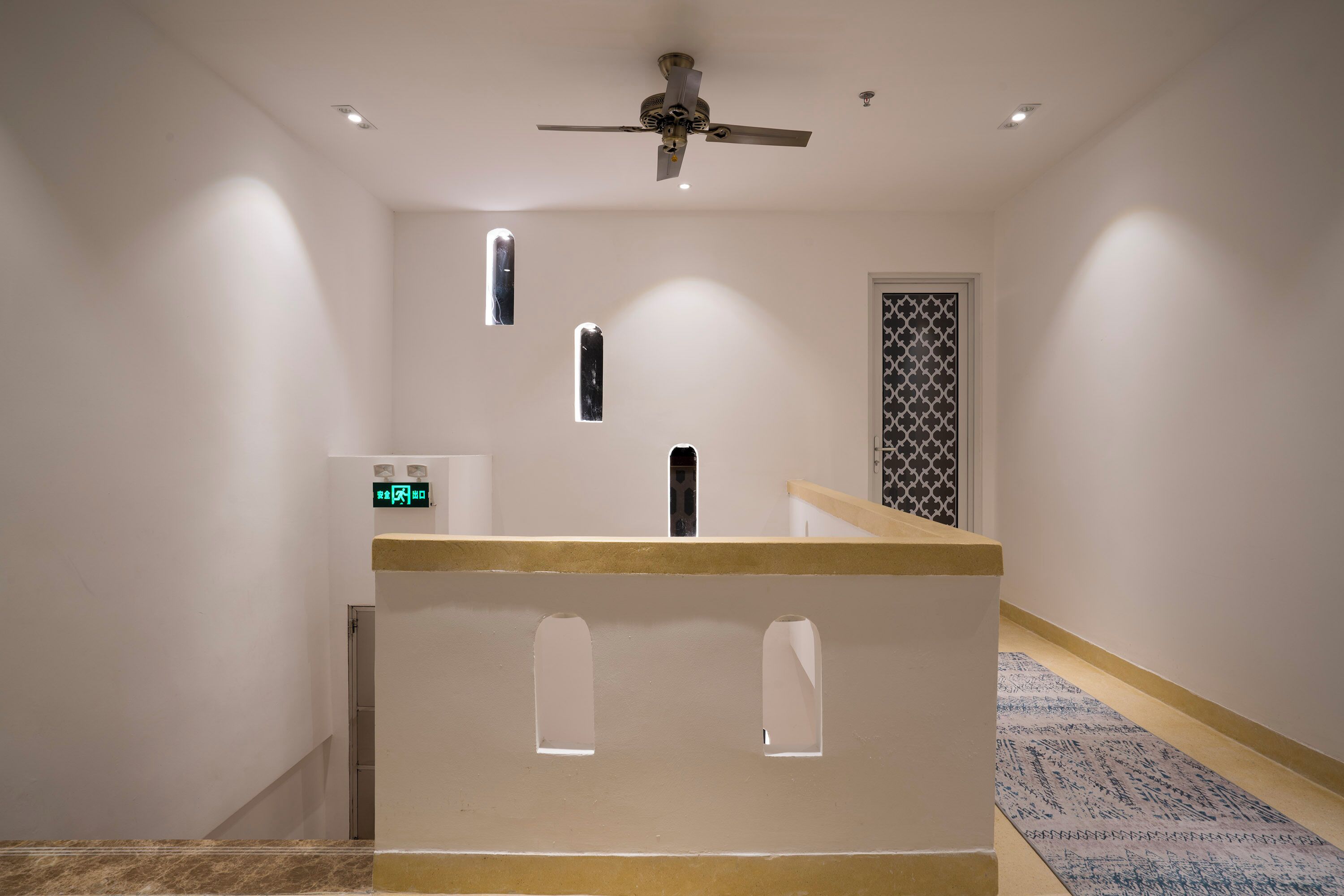 Passadís d'hotel amb una recepció, un ventilador de sostre i una porta amb un disseny.