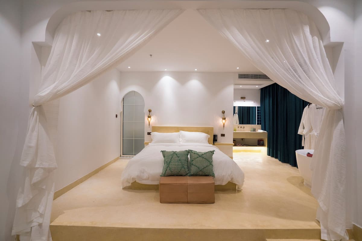 Un dormitorio con una cama grande, un banco y un baño visible al fondo.