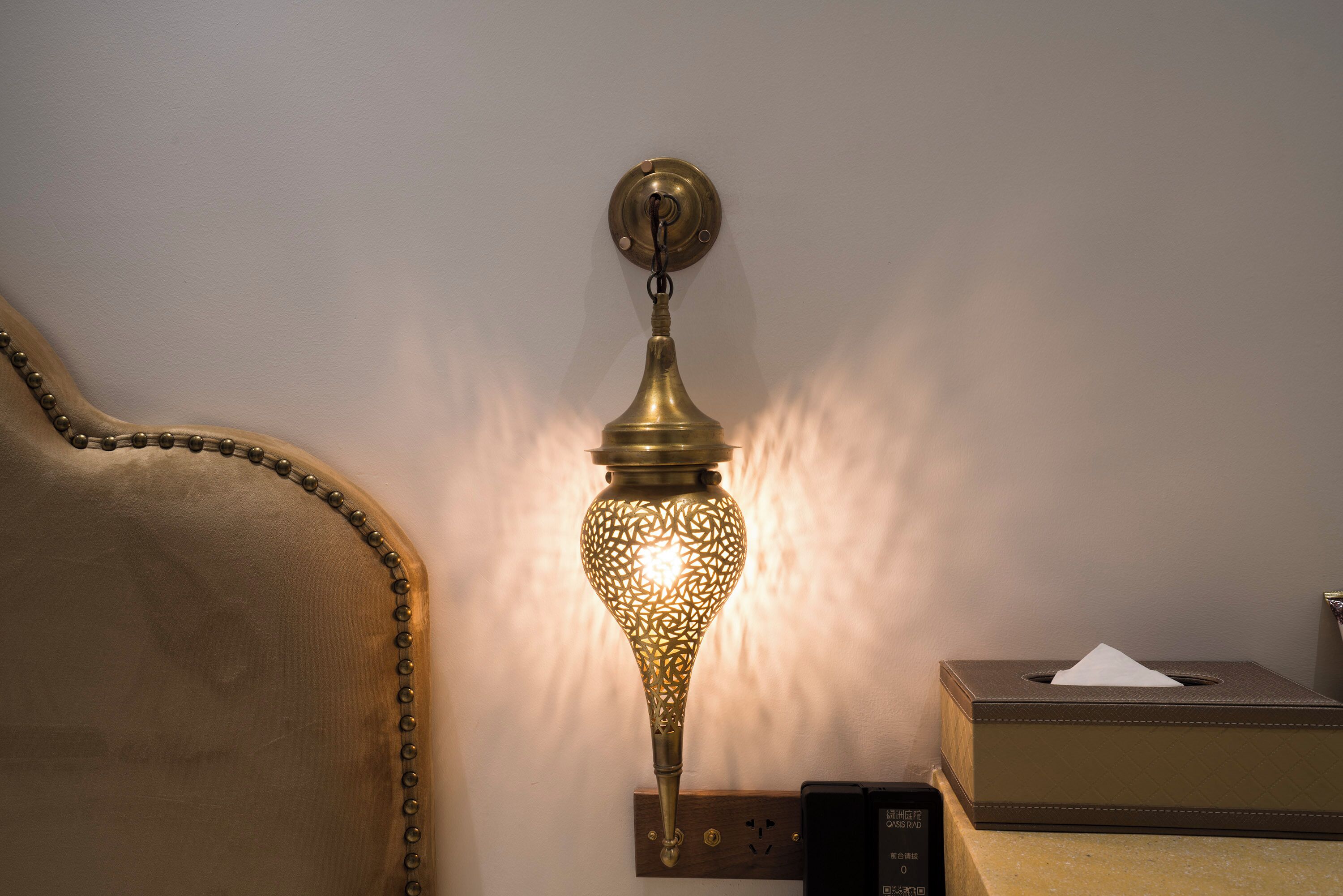 A wall-mounted brass lamp with intricate patterns, a plush brown sofa, and a tissue box on a wooden surface.