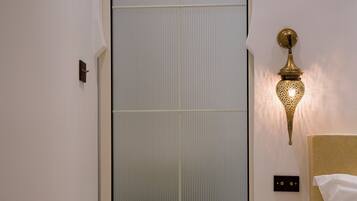Una habitación con puerta corredera, cama con ropa blanca, lámpara de pared y un estante pequeño.