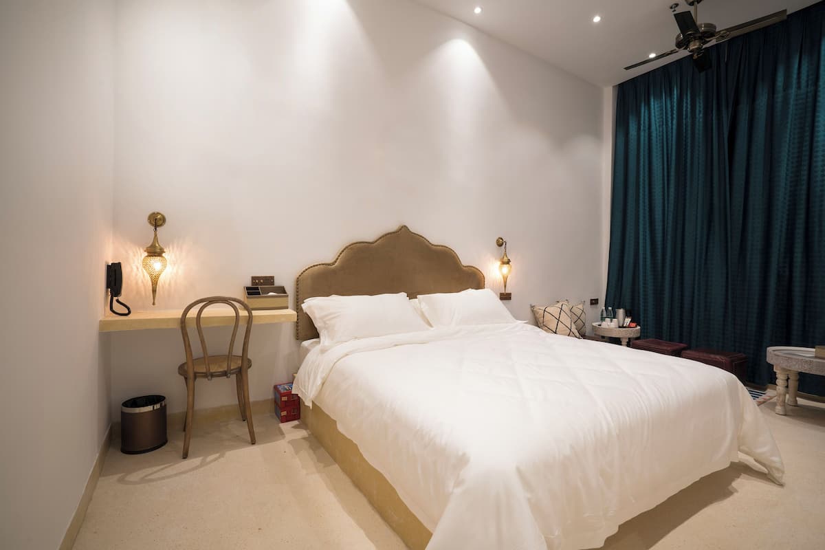 Un dormitorio ordenado con una cama grande, un escritorio con una silla, una mesita y un cubo de basura.