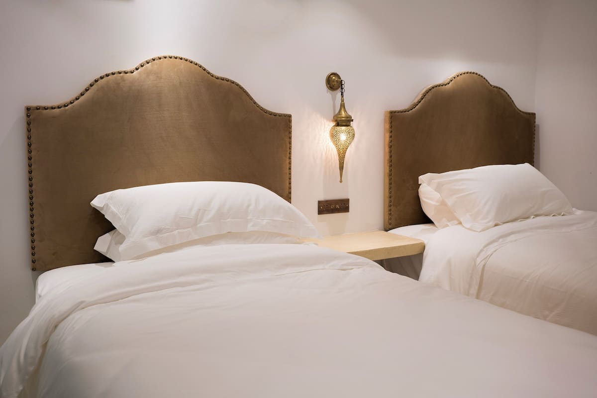 Una habitación de hotel con dos camas, una mesita de noche y una lámpara de pared.