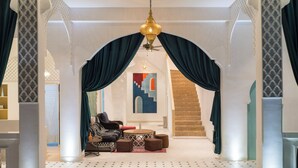 Un interno lussuoso con soffitto alto, un lampadario, una zona relax con divano e pouf, e una scalinata con ringhiere decorate.