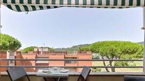 Un balcón con una mesa lista para dos personas, con vistas a una zona residencial con árboles y edificios.