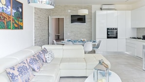A modern living room with a white sofa, a dining area with a round table, and a kitchen with white cabinets and a black stove. - Beautiful  villa for 6 people with A/C, WIFI, terrace and pets allowed (Castiglione Della Pescaia)