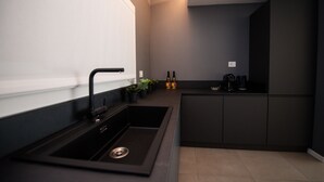 Een moderne keuken met een zwarte spoelbak, donkere kastjes en een klein aanrecht met planten en flessen.