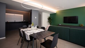 Een moderne eetruimte met een tafel gedekt voor vier personen, een groene bank en een flatscreen televisie aan de muur.