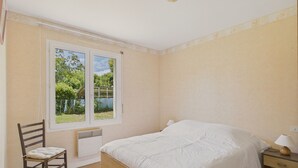 Un dormitorio con una cama individual, una silla, una mesita de noche con lámpara y una ventana con vistas al exterior.