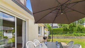 Un patio con mesa y sillas, una sombrilla y vistas a una casa y follaje.