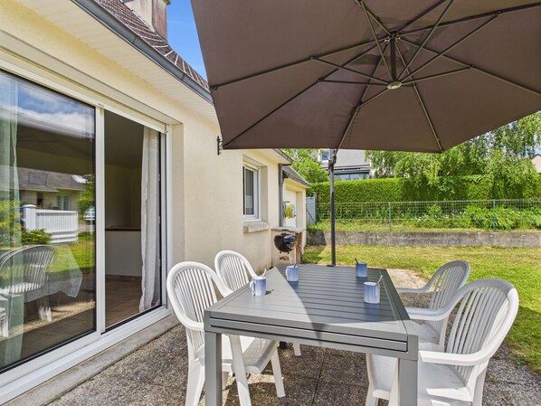 A patio with a table and chairs, an umbrella, and a view of a house and greenery. - Single-storey house for 4 – garden and terrace (La Forêt-Fouesnant)