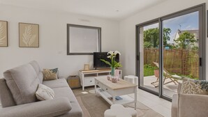 A modern living room with a sofa, coffee table, and TV. There is a sliding glass door leading to a balcony with outdoor furniture. - Lovely family home for 8 with garden (Erquy)