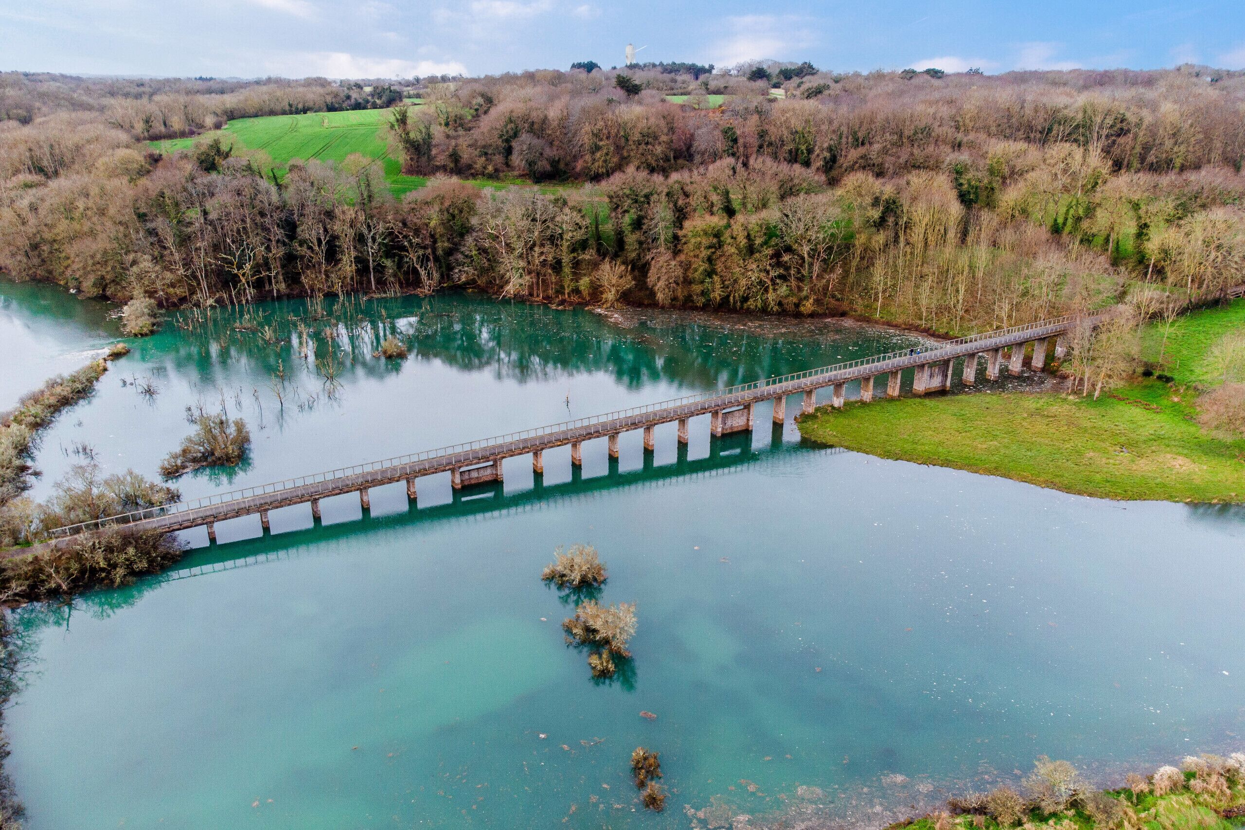 Een brug over een rivier, met groene oevers en heuvels in de verte.