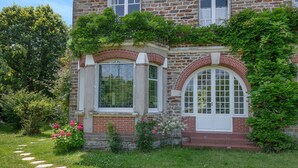 A stone building with a brick facade, large arched windows, and a garden with stepping stones and flowering plants. - Charming villa 250m from beach – sleeps 14 (Saint-Michel-Chef-Chef)