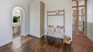 A room with a wooden bench, a coat rack, and a view through an archway to a balcony. - Charming villa 250m from beach – sleeps 14 (Saint-Michel-Chef-Chef)