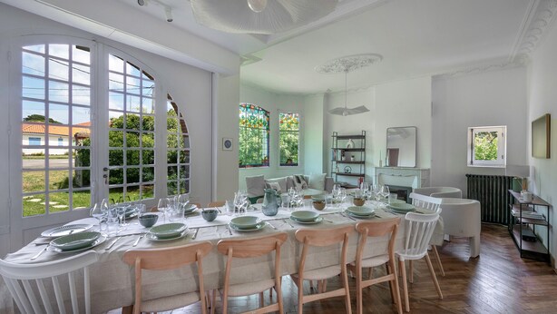 A dining area with a long table set for a meal, large windows with a view of the outside, and a fireplace in the background. - Charming villa 250m from beach – sleeps 14 (Saint-Michel-Chef-Chef)