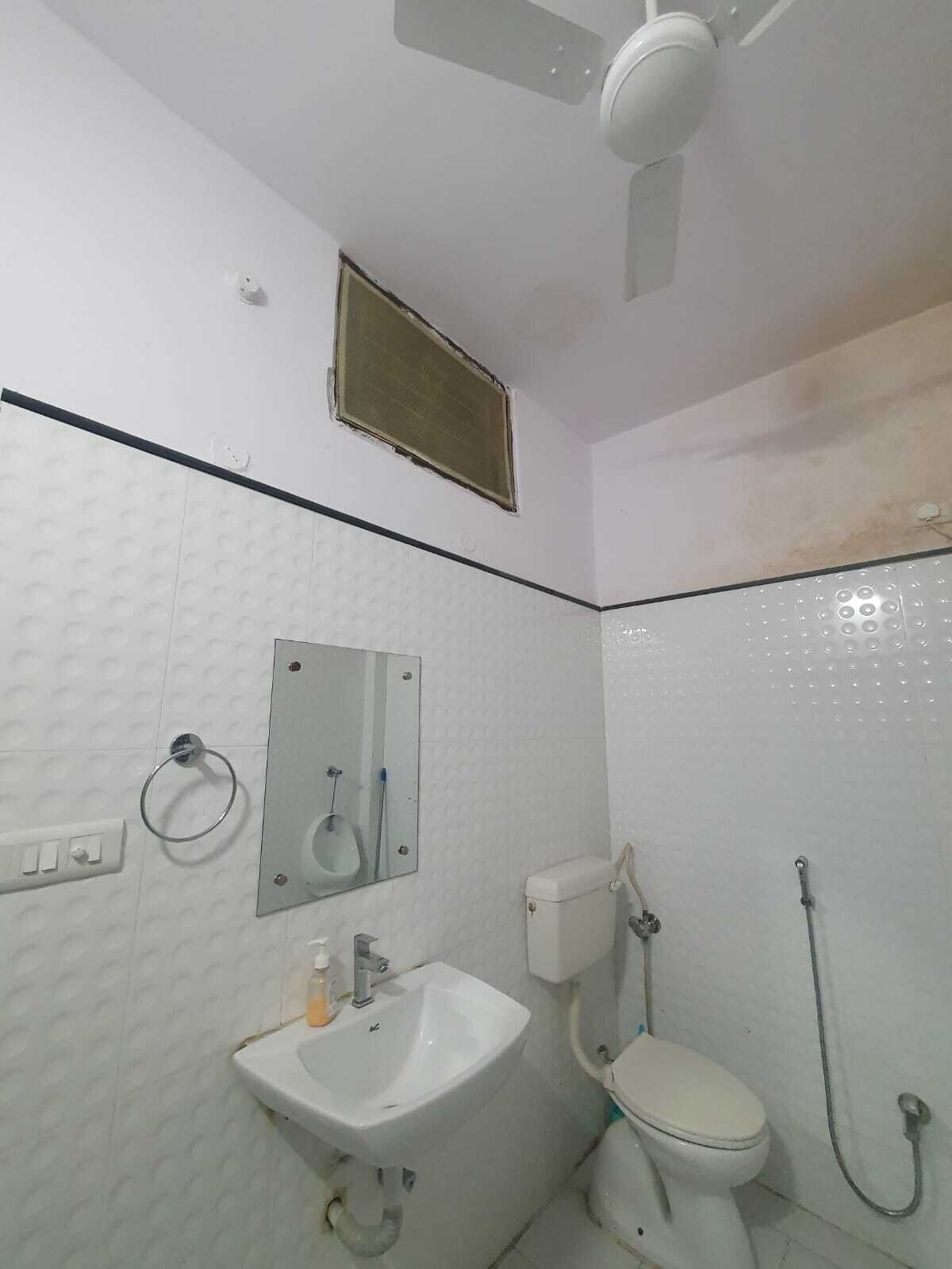 Une salle de bain avec un lavabo, des toilettes et une douche, le tout de couleur blanche. On y trouve un ventilateur de plafond et un miroir au-dessus du lavabo.