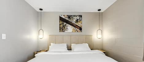 Ein modernes Hotelzimmer mit einem großen Bett, zwei Nachttischen, einem Kopfteil mit integriertem Regal und einem gerahmten Bild an der Wand.