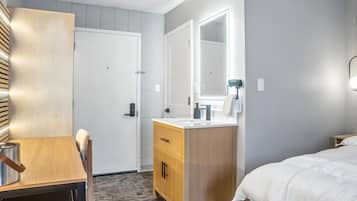 Una habitación de hotel con un escritorio de madera, un tocador con espejo, una cama y una puerta.