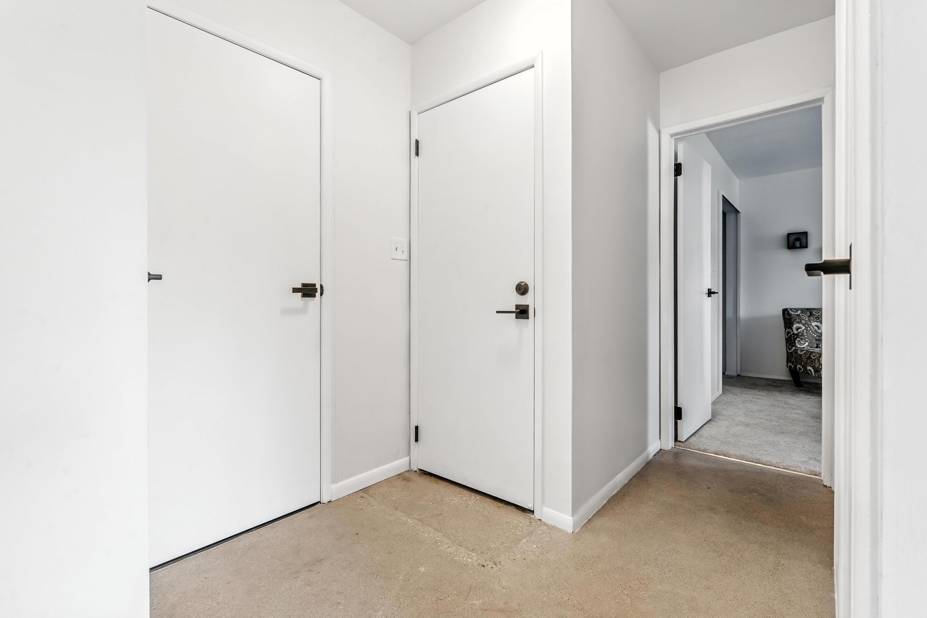Un pasillo con puertas blancas, alfombra color crema y una silla estampada al fondo.